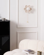 Clérachic flower wall light unlit on a white panelled wall, with a black cabinet and a mug at its side and a boucle sofa below.
