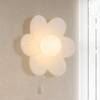 This Clérachic flower wall light glows warmly on a pale wall, its six petals translucent and a gold chain hanging down.