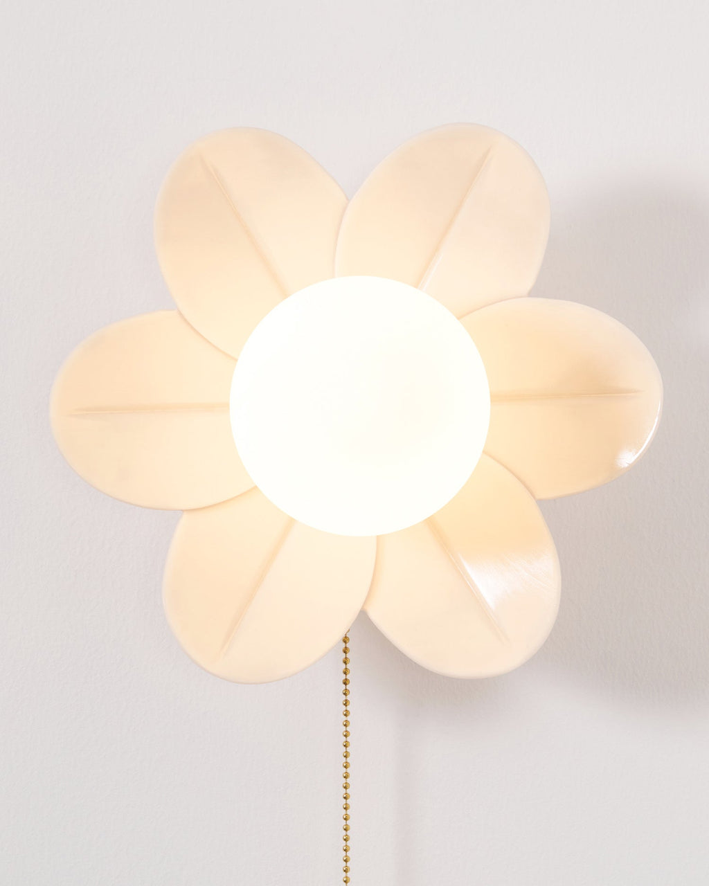 Front view of the lit flower wall light from Clérachic, with a six-petal rim in warm cream and a large frosted globe.
