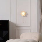 Flower wall light from Clérachic glowing on a moulded white wall, above a black cabinet and the arm of a boucle sofa.