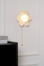 Small lit Clérachic flower wall light on a panelled wall above a black cabinet and magazines, with a cream sofa in the corner.