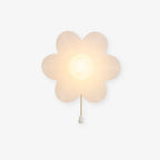 Rounded translucent-white Clérachic flower wall light lit warmly on a plain light backdrop, with a gold chain ending in a white pull.