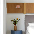 Clérachic's Flowerpot pendant in a soft pink finish, hanging above a bedside table of fresh flowers.