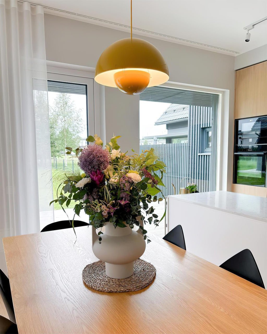Clérachic's Flowerpot pendant in mustard yellow, hung low over a farmhouse table set with flowers.
