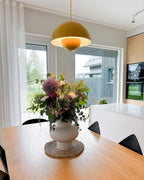 Clérachic's Flowerpot pendant in mustard yellow, hung low over a farmhouse table set with flowers.