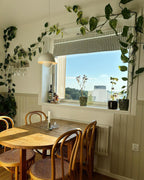 Clérachic's Flowerpot pendant in white, its cord swagged near a window framed by trailing plants.