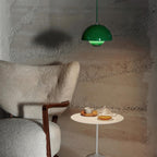 The Clérachic Flowerpot pendant in dark green, glowing softly against a textured plaster wall.