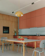 The Clérachic Flowerpot pendant in yellow, plugged in above a dining table in a terracotta kitchen.