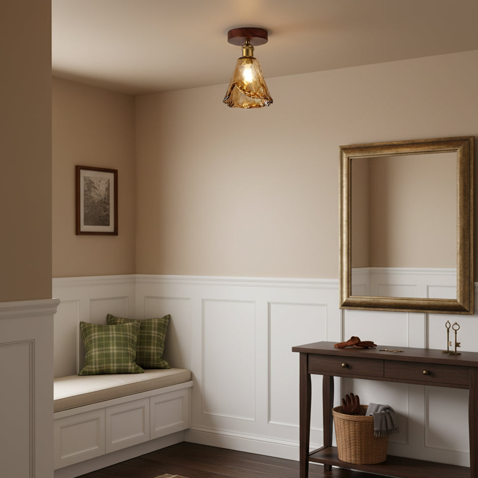 A lit amber glass flush ceiling light from Clérachic above an entry nook with a window seat, a gold-framed mirror and a console table.