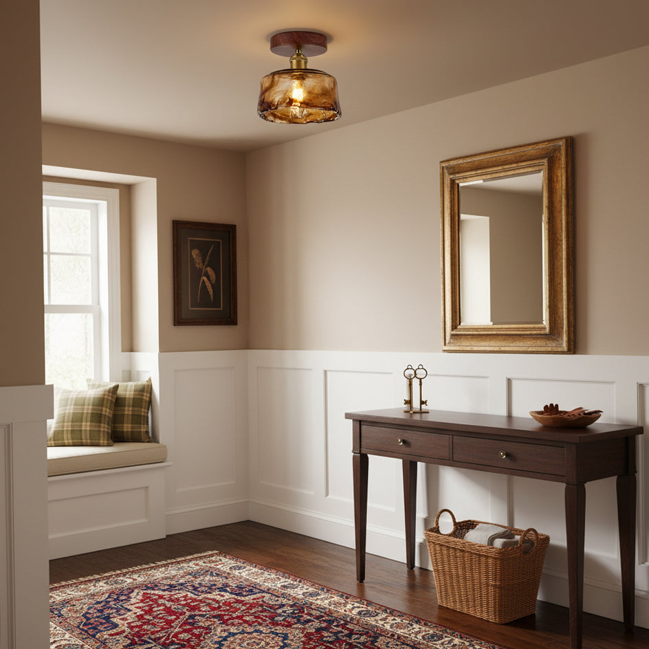 Amber glass flush ceiling light from Clérachic in an entryway with a window seat, a gold mirror and a dark console with a basket.