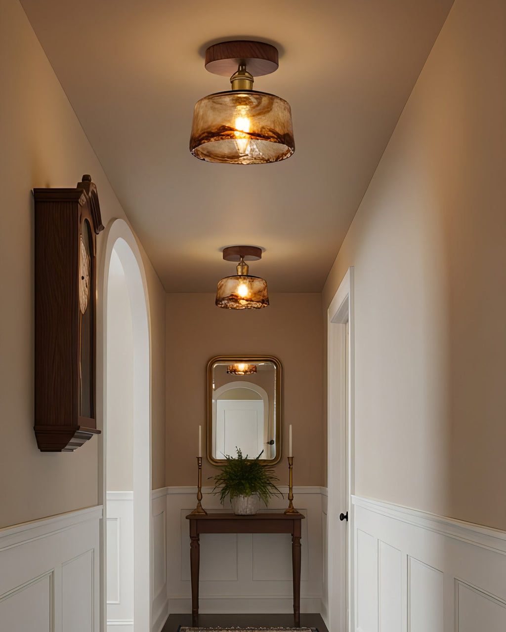 Two lit flush ceiling lights from Clérachic with amber glass shades in a narrow hallway with a wall clock and a mirror at the end.