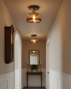 Two lit flush ceiling lights from Clérachic with amber glass shades in a narrow hallway with a wall clock and a mirror at the end.