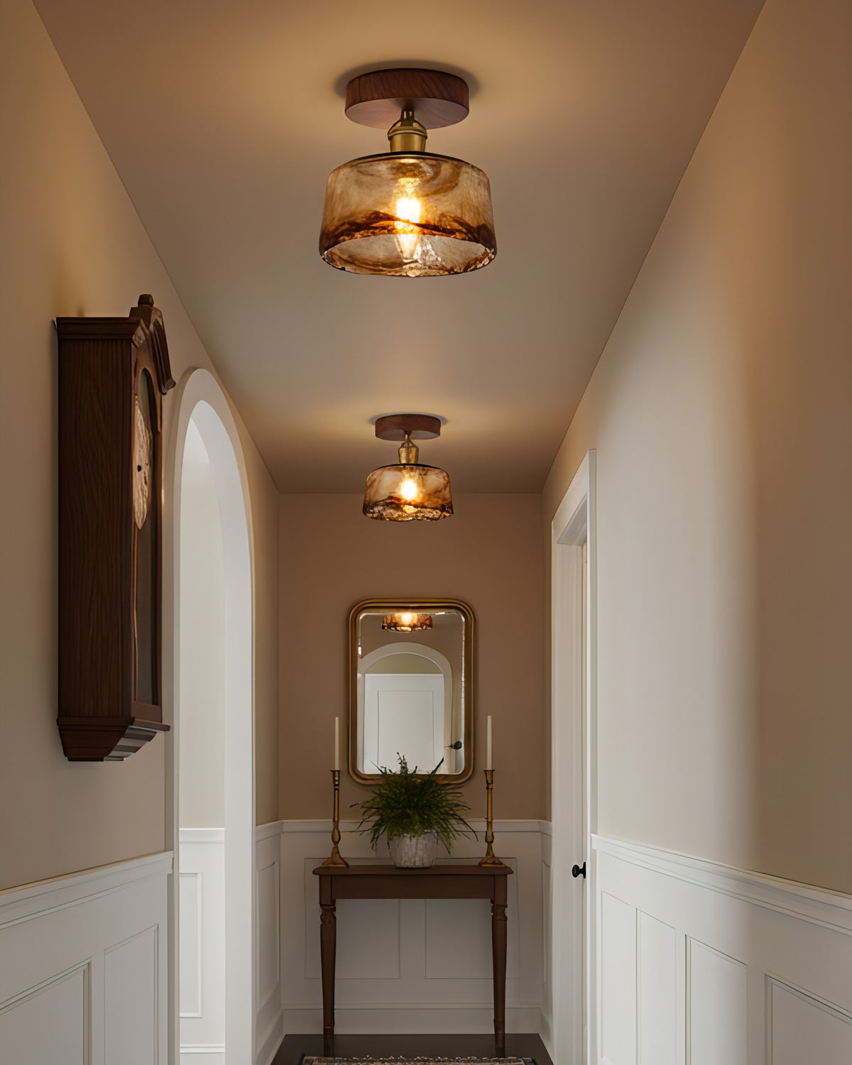 Two lit flush ceiling lights from Clérachic with amber glass shades in a narrow hallway with a wall clock and a mirror at the end.