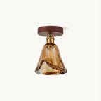 Flush ceiling light from Clérachic with a flared amber glass shade, brass socket and round walnut-effect canopy, on a plain backdrop.
