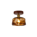 A lit Clérachic flush ceiling light with a wide, flat amber glass shade with a swirled finish, on a round walnut-effect canopy.