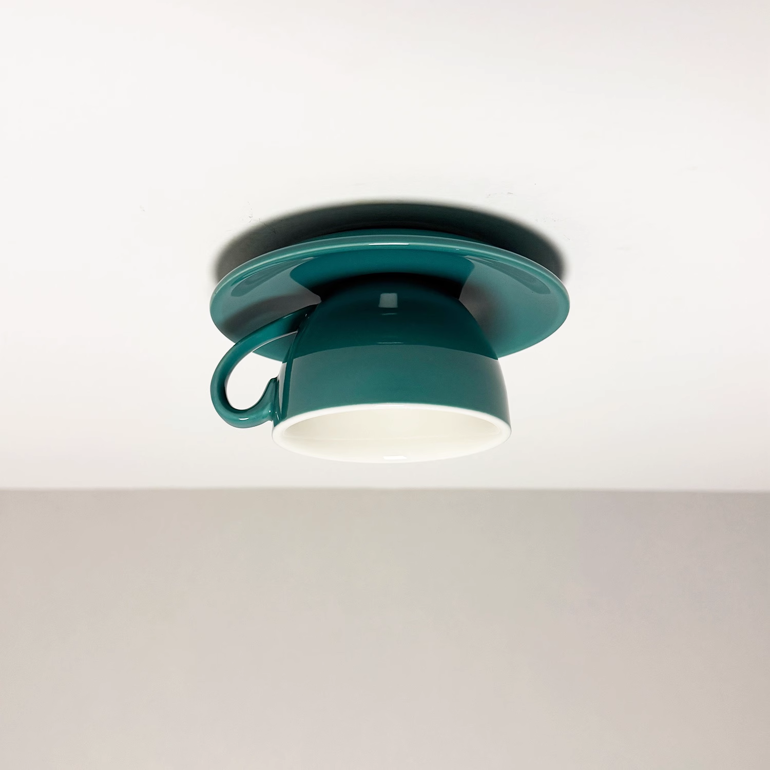 The Clérachic peacock green coffee-cup light highlights its glossy saucer and silhouette.