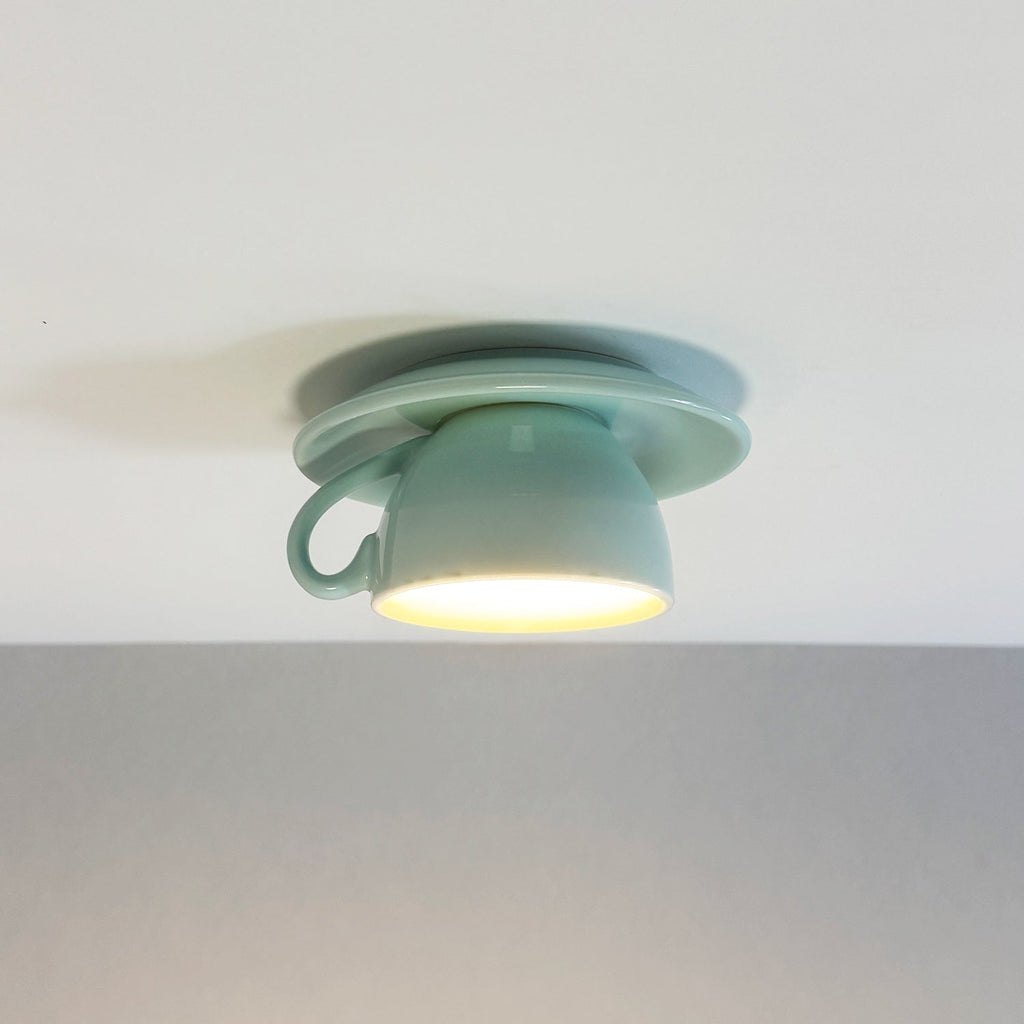 Clérachic's light blue coffee-cup ceiling light glows warm against a plain gray wall.