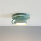 Clérachic's light blue coffee-cup ceiling light glows warm against a plain gray wall.
