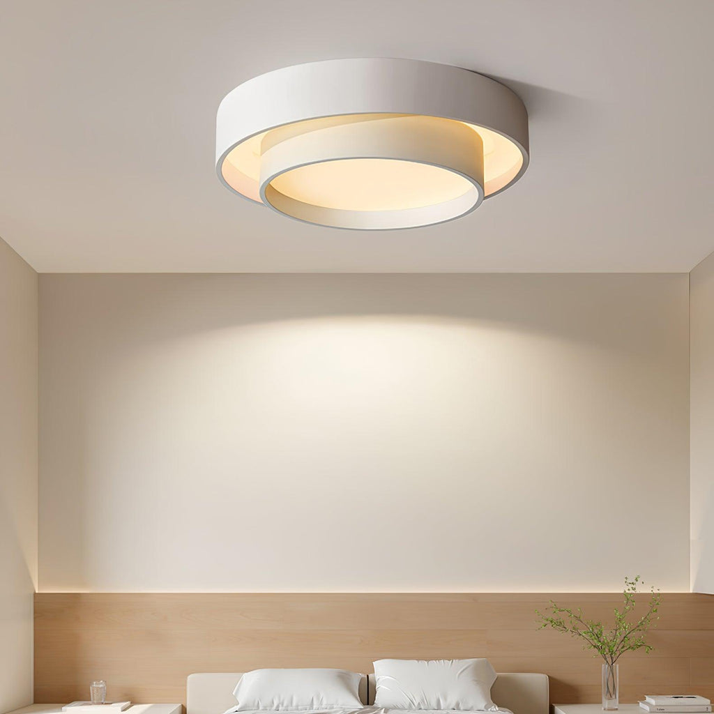 The Clérachic double-ring ceiling light glows warm above a bed dressed in linen with a plant.