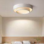 The Clérachic double-ring ceiling light glows warm above a bed dressed in linen with a plant.