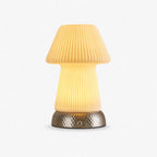 Glowing mushroom-shaped lamp in fluted translucent ceramic on a hammered metal base, this Clérachic table lamp on a plain light backdrop.