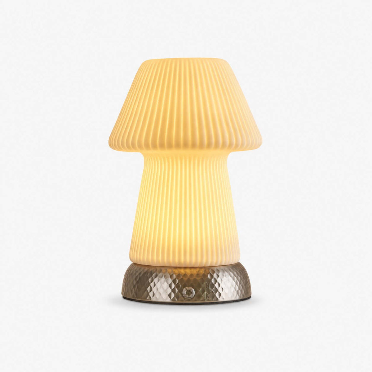 Glowing mushroom-shaped lamp in fluted translucent ceramic on a hammered metal base, this Clérachic table lamp on a plain light backdrop.