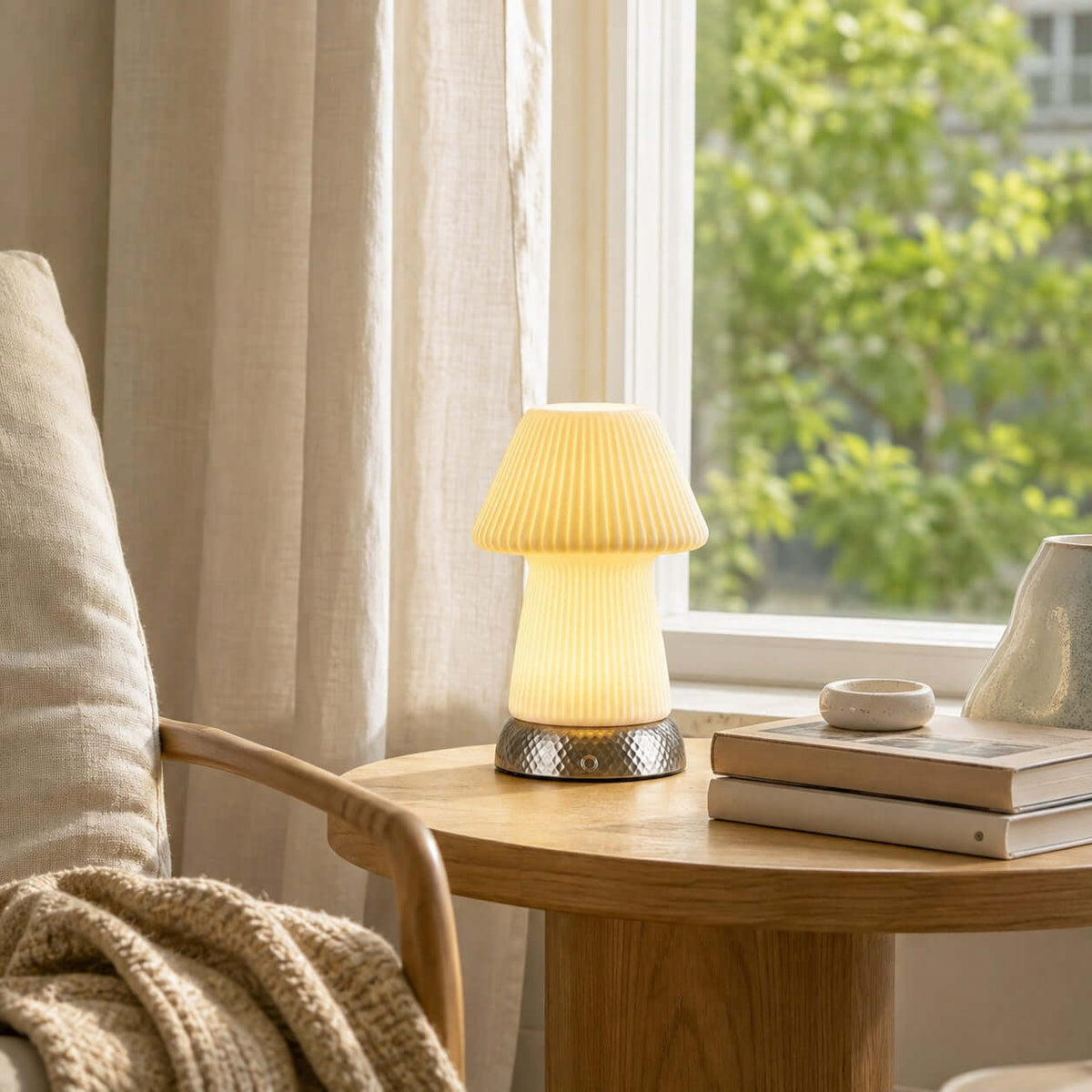 Set on a small round wooden table by a sunlit window with leafy trees outside, this Clérachic lamp sits near a stack of books and a knitted throw.