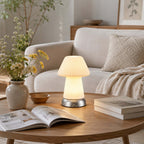 Lit on a round coffee table beside an open magazine and wild flowers in a vase, this Clérachic lamp stands before a cream armchair.