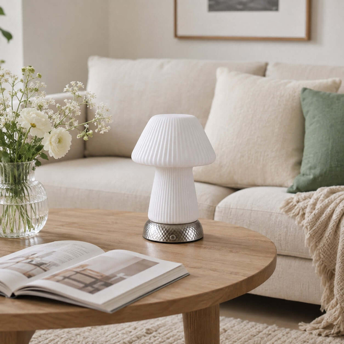 Unlit, this white fluted Clérachic lamp stands on a wooden coffee table before a cream sofa, with a magazine and a jar of white flowers.