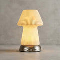 Close view of the fluted ceramic shade glowing warm over the hammered metal base of this Clérachic lamp, on a grey plaster backdrop.