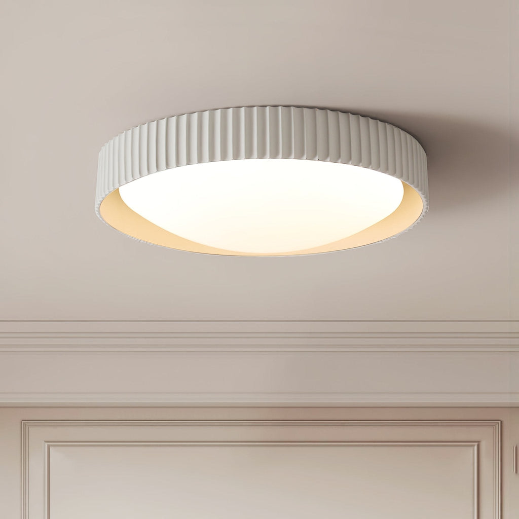 Seen from below on a panelled ceiling, a Clérachic ribbed flush light in pale grey with a glowing white diffuser and a soft cream inner edge.