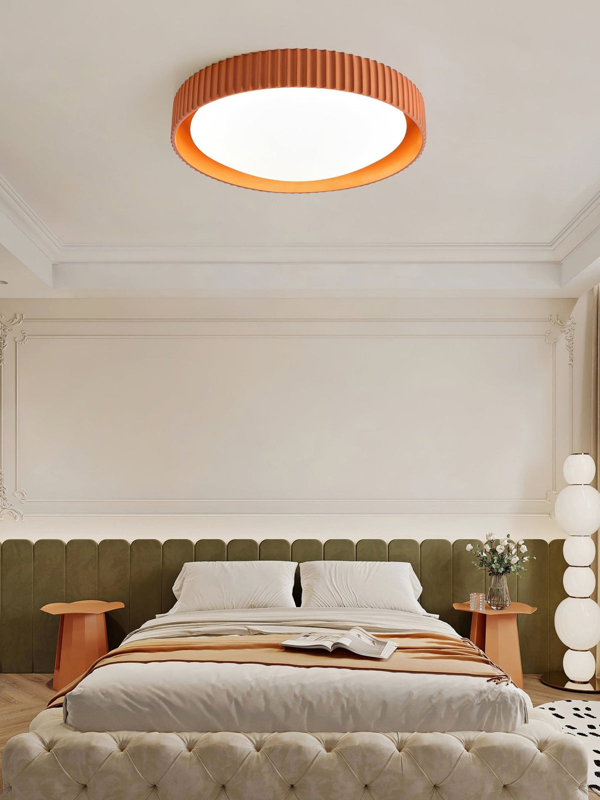 In a bedroom with an olive padded headboard and orange side tables, a Clérachic orange ribbed flush ceiling light sits above a cornice.