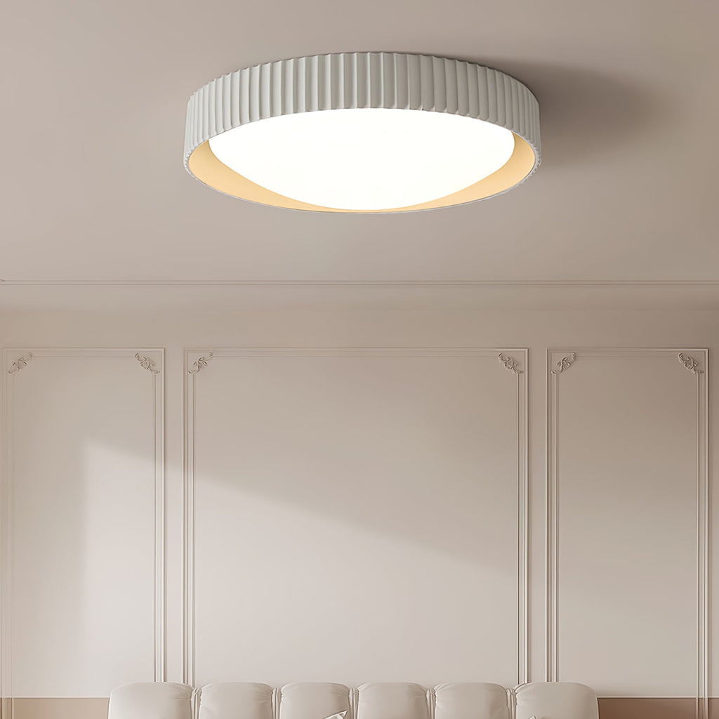 A pale grey Clérachic flush ceiling light above a panelled wall with a cream bench below, its ribbed rim and white diffuser lit.