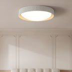 A pale grey Clérachic flush ceiling light above a panelled wall with a cream bench below, its ribbed rim and white diffuser lit.