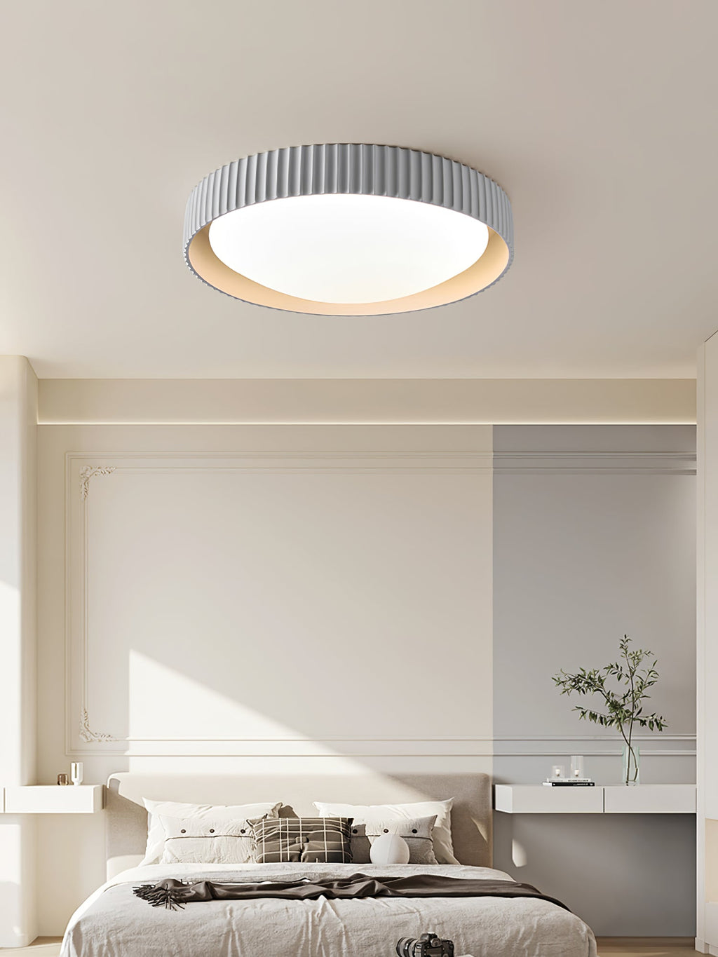 Over a bed with a white headboard and shelf, a pale grey Clérachic flush ceiling light with a ribbed edge sits centred on the ceiling.