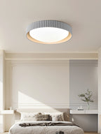 Over a bed with a white headboard and shelf, a pale grey Clérachic flush ceiling light with a ribbed edge sits centred on the ceiling.