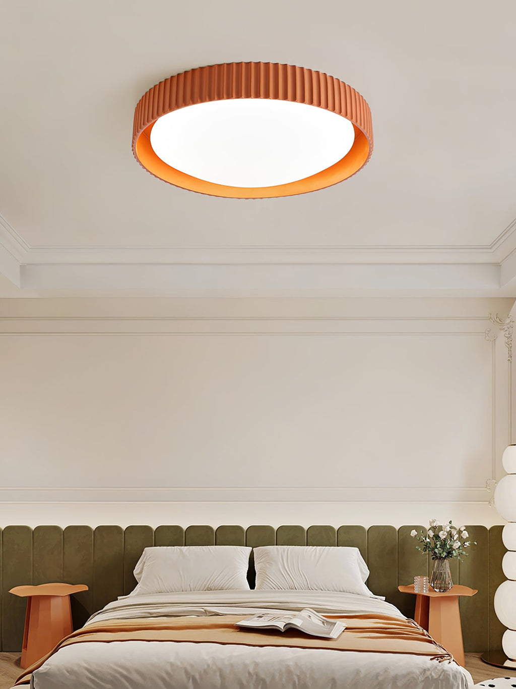 Close view of an orange Clérachic ribbed flush light lit above a bed with olive padding and a peach throw.
