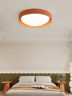 Close view of an orange Clérachic ribbed flush light lit above a bed with olive padding and a peach throw.