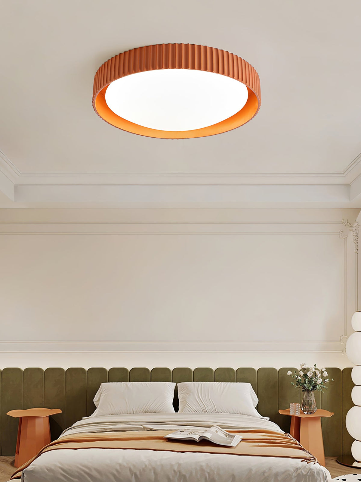 Close view of an orange Clérachic ribbed flush light lit above a bed with olive padding and a peach throw.