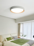 A grey Clérachic ribbed flush ceiling light above a bedroom with sheer curtains, a white bed and a green throw.