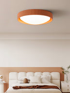 Orange Clérachic flush ceiling light, its ribbed rim and white diffuser lit, above a cream bed against a terracotta panel.