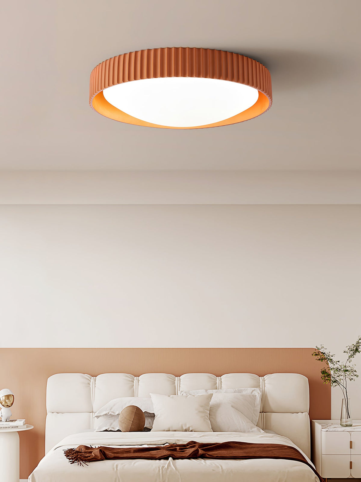 Orange Clérachic flush ceiling light, its ribbed rim and white diffuser lit, above a cream bed against a terracotta panel.