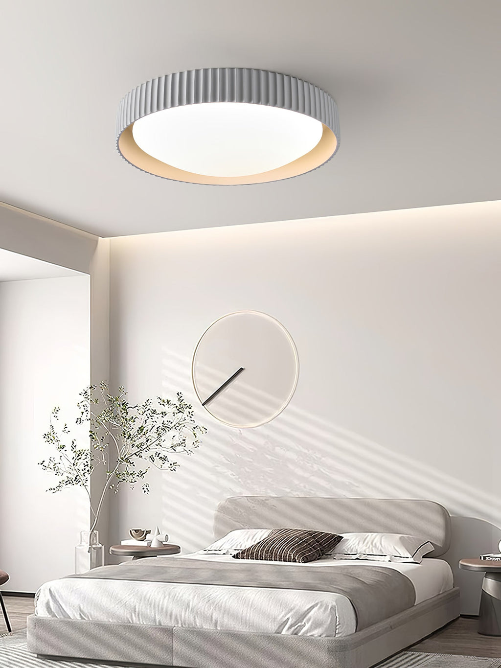 Over a grey bed beneath a wall of soft cove lighting, a pale grey Clérachic ribbed flush ceiling light sits above a round wall mirror.