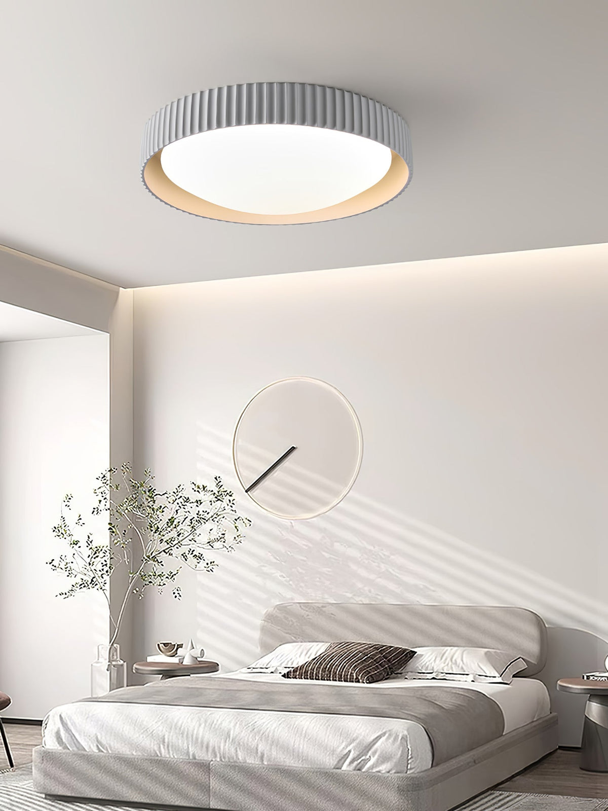 Over a grey bed beneath a wall of soft cove lighting, a pale grey Clérachic ribbed flush ceiling light sits above a round wall mirror.