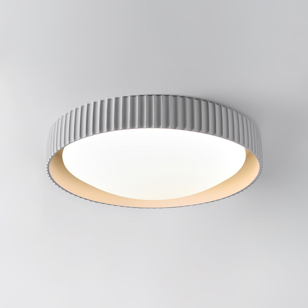 Close view of the fine vertical ribs and round white diffuser on this pale grey Clérachic flush ceiling light, against a grey wall.