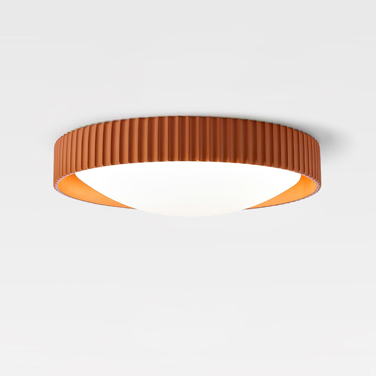 An orange Clérachic flush ceiling light on a pale backdrop, its ribbed rim in burnt orange around a smooth white diffuser.