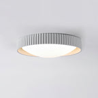 A pale grey Clérachic flush ceiling light seen from below, its ribbed drum rim sitting low and flat to a light grey ceiling.