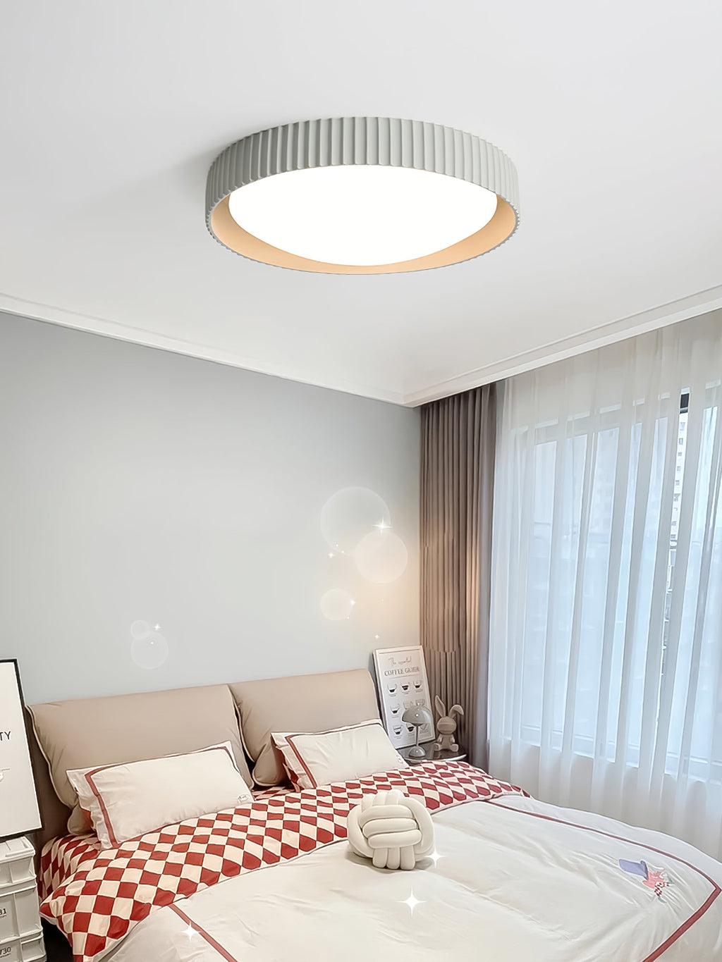 In a bedroom with a checked red and white duvet and sheer curtains, this grey Clérachic flush ceiling light is fitted to a white ceiling.