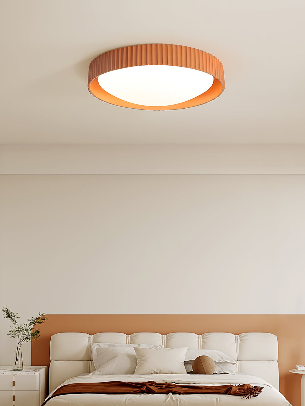Above a cream bed headboard on a peach wall, an orange Clérachic ribbed flush ceiling light sits flat to the ceiling.