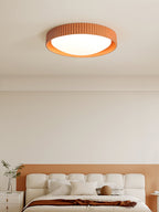 Above a cream bed headboard on a peach wall, an orange Clérachic ribbed flush ceiling light sits flat to the ceiling.